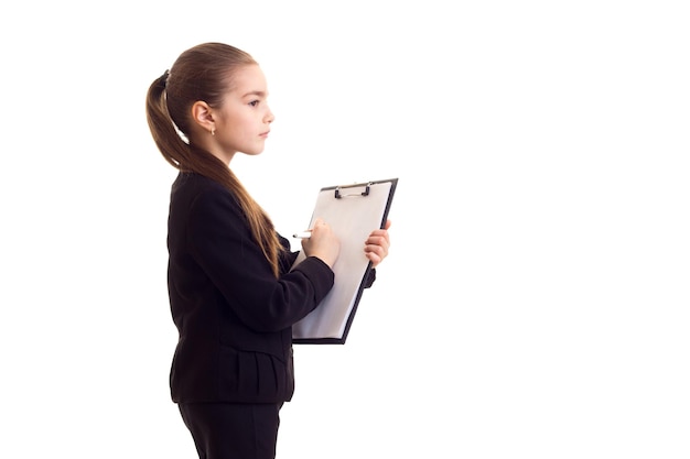 Little smiling girl with long brown ponytail in white Tshirt and black jacket holding black folder