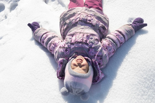 冬の日に雪の上に横たわる笑顔の幸せな女の子