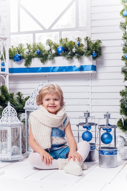 Little smiling pretty girl sitting next to a Christmas tree 