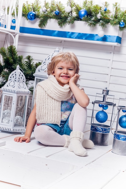 Little smiling pretty girl sitting next to a Christmas tree