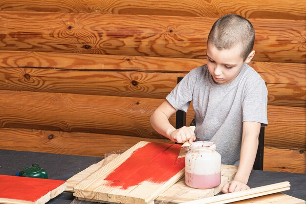 Little smiling toddler boy paints a tree with a brush in hand in red