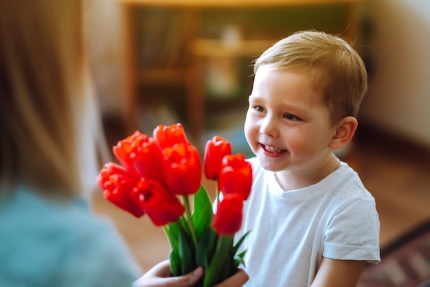 幼い息子は母を祝福し、花のチューリップの花束を与えます。母の日おめでとう。