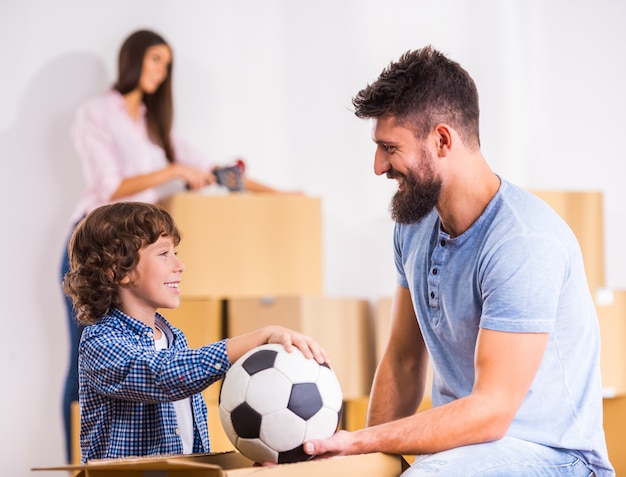 Little son and his dad are holding a soccer ball.