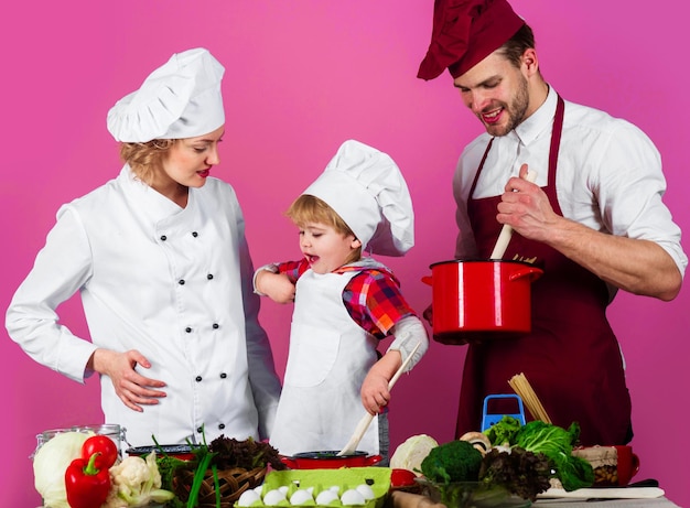 Piccolo figlio e genitori in cappelli da chef in cucina famiglia che cucinano insieme a casa uno stile di vita sano