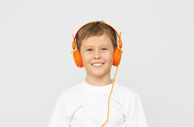 ヘッドフォンを着用し、音楽を聴き、目を閉じて立って白い背景の上に隔離されたスポーツウェアの小さなスポーツ少年の子供。スポーツ、アクティブなライフスタイルのコンセプト。横ショット