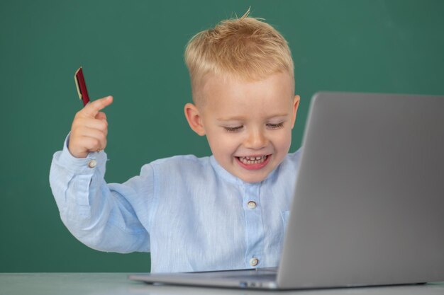 Little student boy using laptop computer in school class