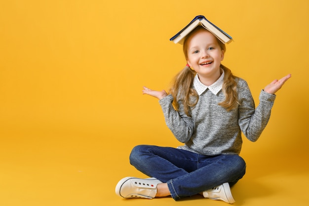 Little student girl is sitting with a book on her head