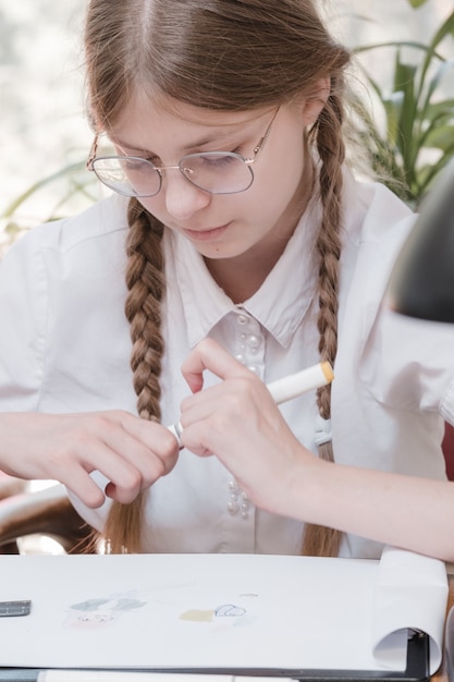 学校で勉強している小さな学生の女の子。ホーム趣味。家で絵を描いている子供の女の子の笑顔。教師から教育を受けるか、両親と一緒に家で学び、勉強するか。宿題をしている少女。