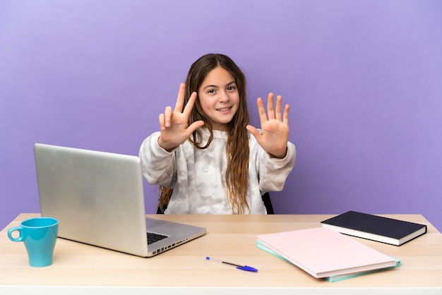 Piccola studentessa in un posto di lavoro con un laptop isolato su sfondo viola che conta otto con le dita