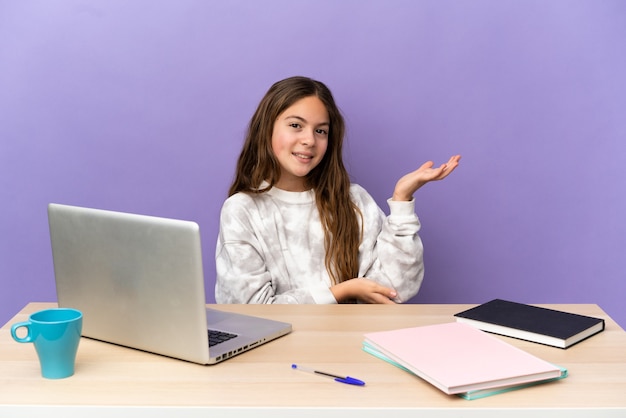 Piccola studentessa in un posto di lavoro con un laptop isolato su sfondo viola che allunga le mani di lato per invitare a venire