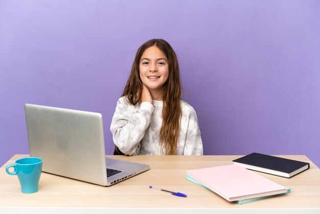 Piccola studentessa in un posto di lavoro con un laptop isolato su sfondo viola che ride