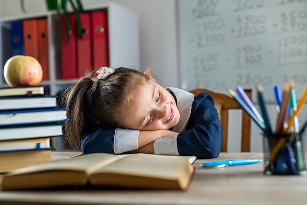 Photo little student is sleeping on the school desk because she is tired