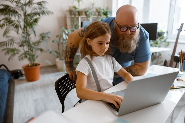 Little student works on laptop while daddy stands nearby at home