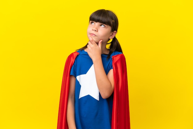 Little super hero kid isolated on purple background having doubts and with confuse face expression