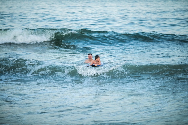 어린 서퍼는 바다 파도에서 서핑 보드를 타는 법을 배웁니다. 아버지와 아들이 여름 바다에서 서핑을 배우며 놀고 있습니다. 어린 소년이 서핑 보드에서 수영합니다.