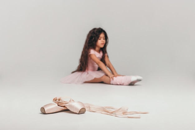 Little swarthy ballerina dancer in a pink tutu academy student posing on white background