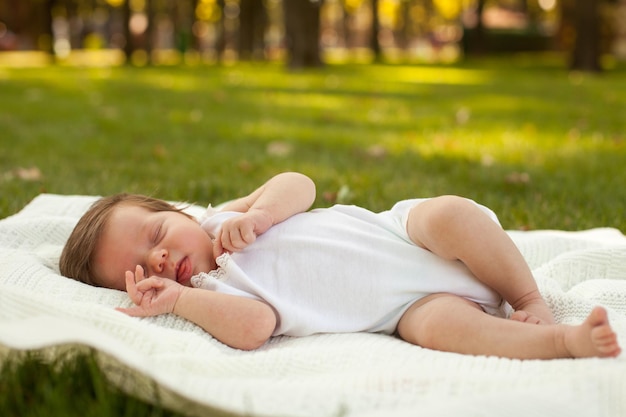 Little sweet baby in white clothing sleeping on the white blanket on the grass