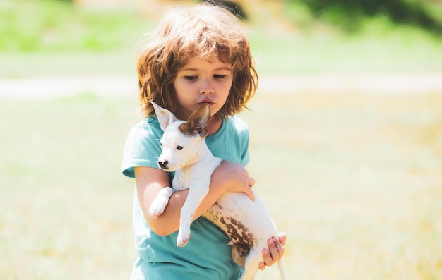 Little sweet curly blonde boy with a white puppy on hands puppies and kid outdoor