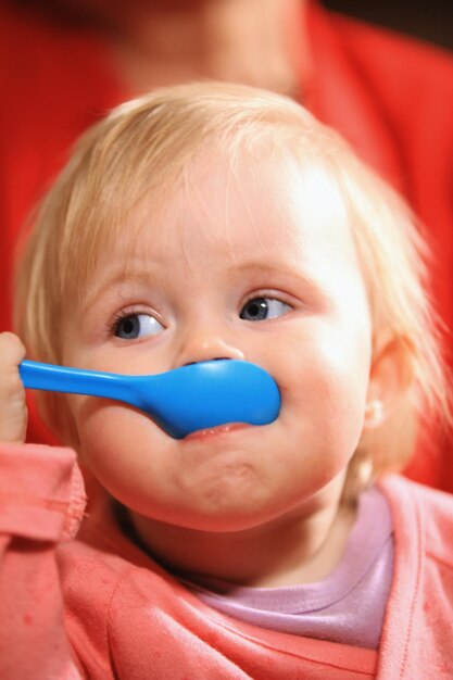 Photo little sweet toddler girl with blue spoon during breakfast, close up