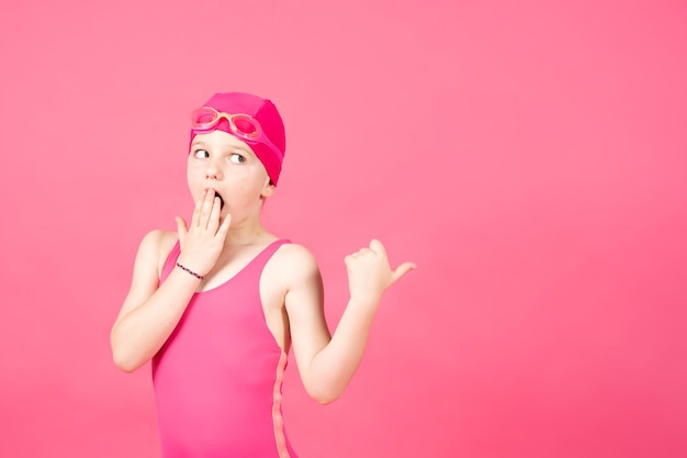 Little swimmer girl hand on mouth pointing at copy space