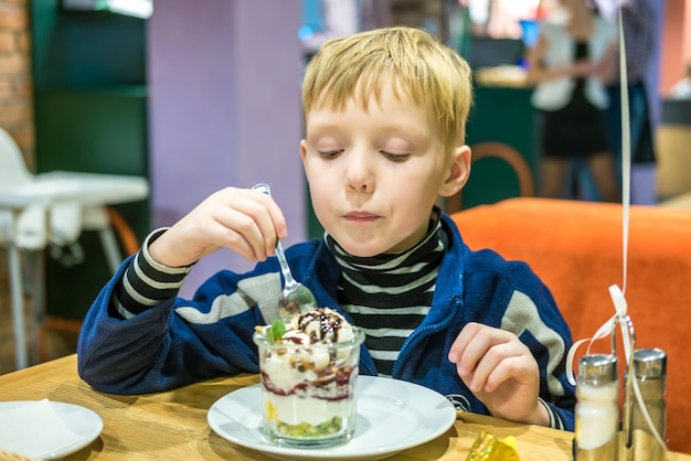 Little teen boy eating dessert ice cream in cafe