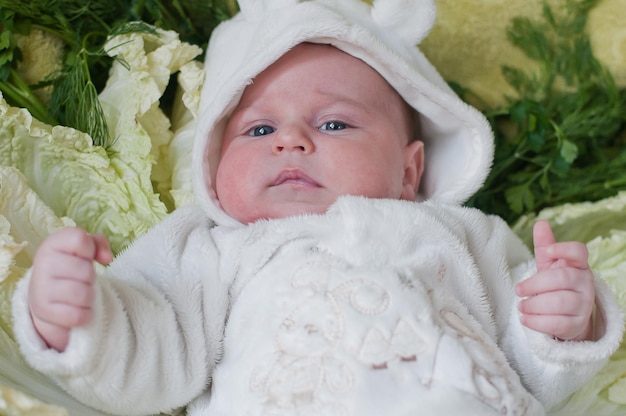 Photo little thoughtful baby lays on cabbage leaves