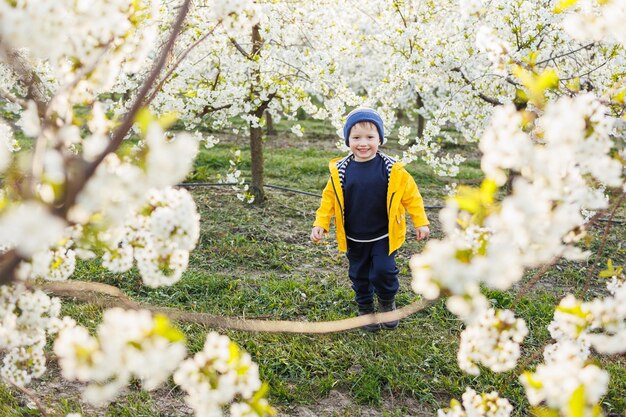 A little threeyearold joyful boy runs on the grass in a blooming garden in the spring Children emoticon of joy happy smiling child