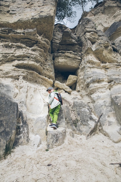 Little toddler boy with backpack climbing by rock