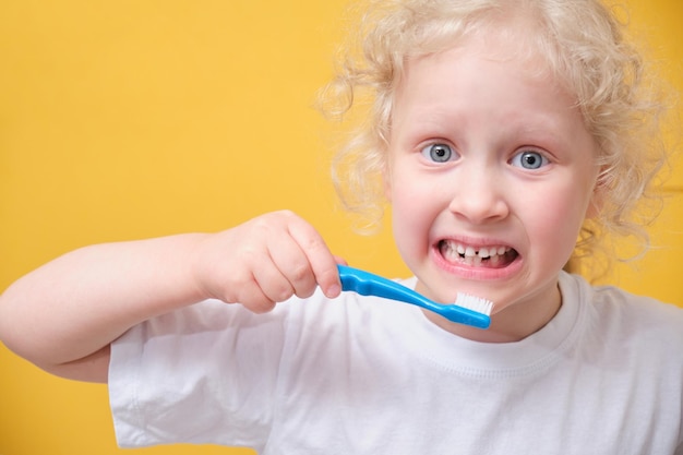 Little toddler girl 6 years old holding toothbrush in hand\
brushing tooth yellow background