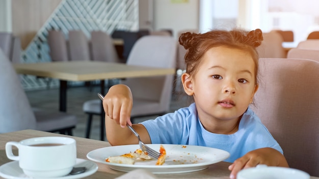 La piccola bambina in maglietta blu mangia una pizza deliziosa