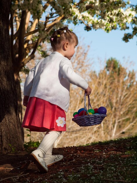 Little toddler girl on Easter egg hunt in urban park.