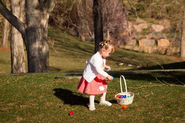 Little toddler girl on Easter egg hunt in urban park.