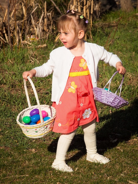 Little toddler girl on Easter egg hunt in urban park.