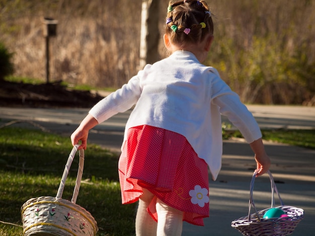 Little toddler girl on Easter egg hunt in urban park.