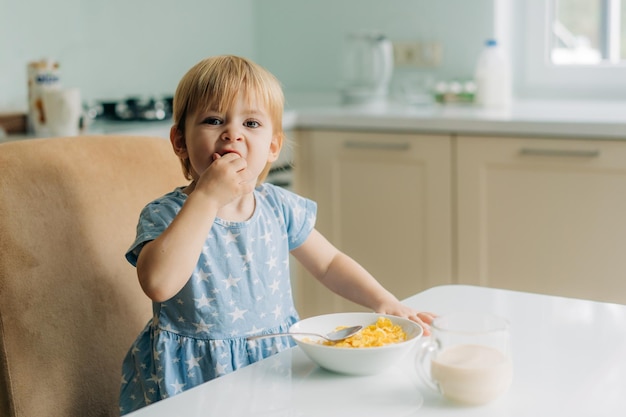 幼い女の子が朝にキッチンでミルクとコーンフレイクを食べる