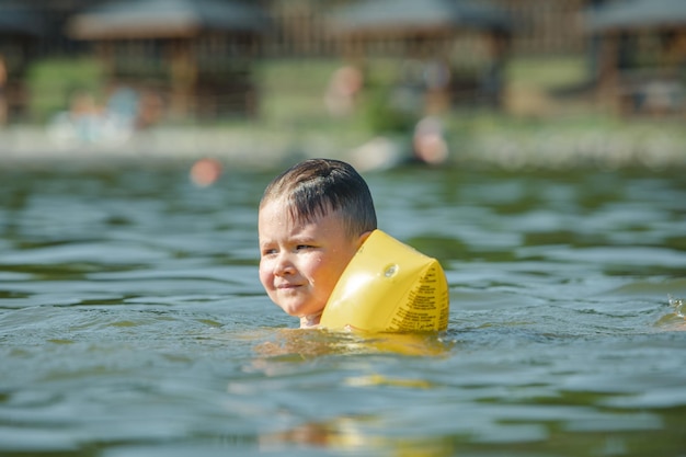 Little toddler kid swimming in lake with inflatable arms aids support