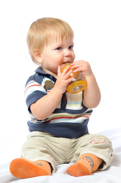 Il piccolo bambino si siede e beve l'acqua dalla bottiglia arancione