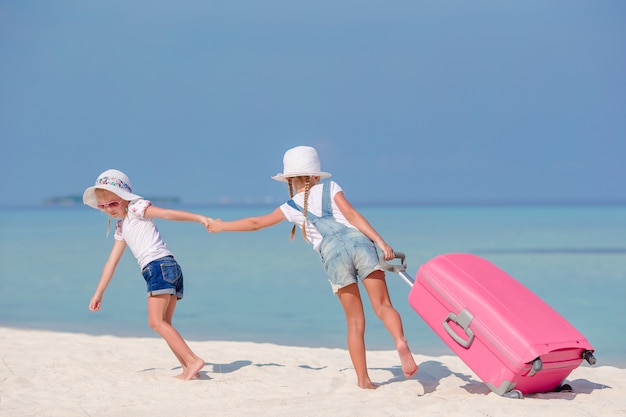 Ragazze dei piccoli turisti con la grande valigia sulla spiaggia bianca tropicale