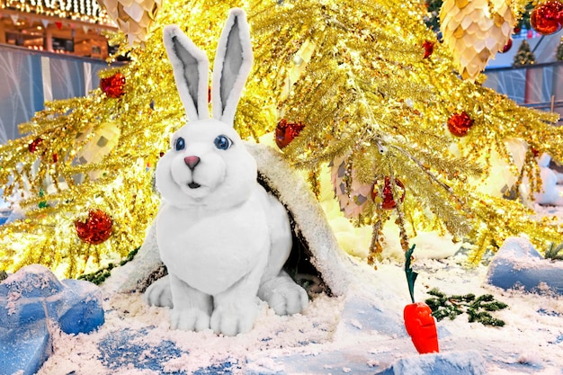 Фото Маленький игрушечный белый кролик сидит под золотой елкой. концепция празднования нового года.
