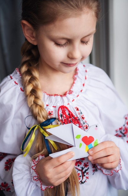 A little Ukrainian girl in traditional clothes holds a paper dove of peace in her hands Support for Ukraine Stop the war