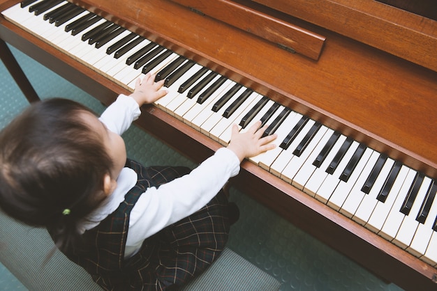 Foto piccola ragazza ben vestita che gioca sul piano di legno, vista dall'alto