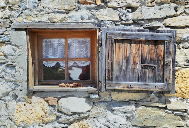 Piccola finestra e persiana su una facciata in pietra di un vecchio chalet alpino