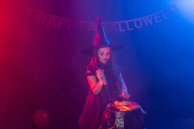 Little witch child cooking potion in the cauldron on halloween