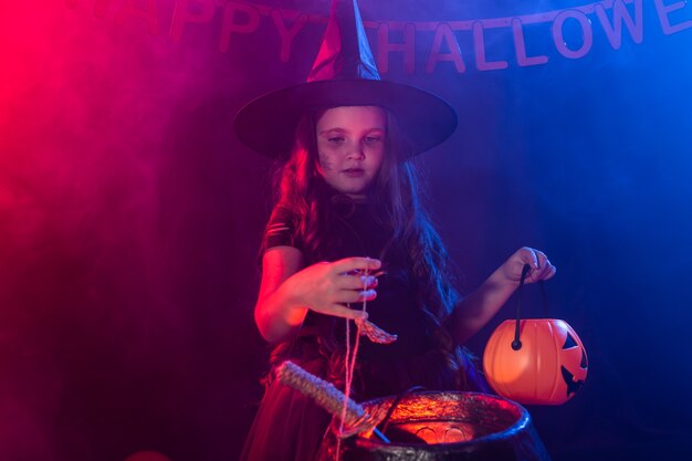 Little witch child cooking potion in the cauldron on Halloween.