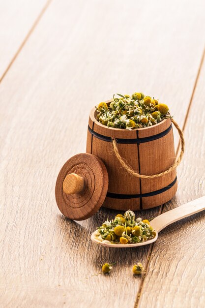 Little wooden barrel and spoon with dry flowers of chamomile on wooden boards.