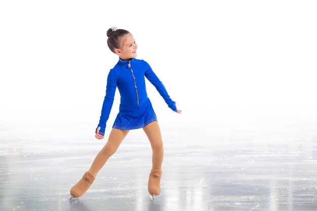 A Little young figure skater posing in blue training dress on ice on white background