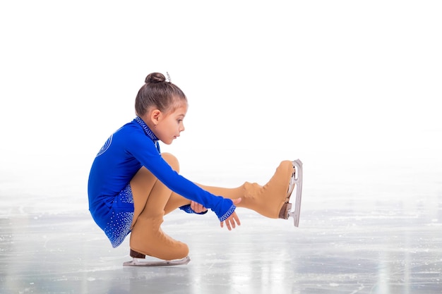 A Little young figure skater posing in blue training dress on ice on white background