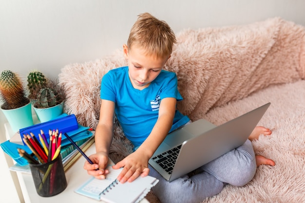 Little young school boy working at home with a laptop and class notes studying in a virtual class. Distance education and learning, e-learning, online learning concept during quarantine