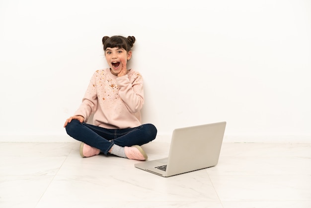 Little young woman with a laptop sitting on the floor with surprise and shocked facial expression