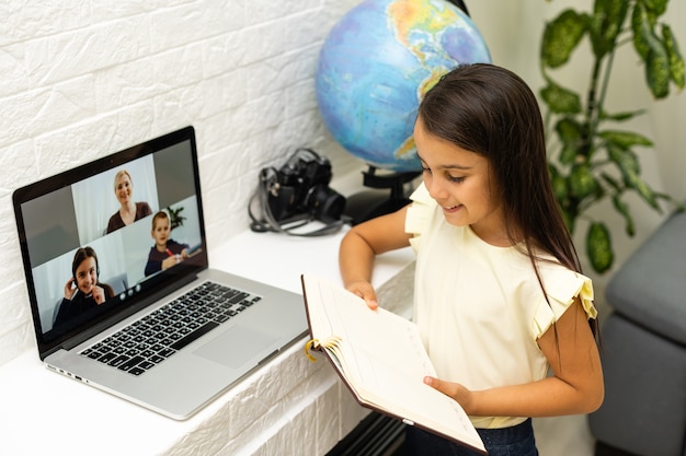 사진 놀라움과 흥분의 표정으로 노트북 화면을 보고 있는 어린 소녀. 메모를 하는 똑똑하고 웃는 어린 소녀. 비즈니스 개념의 통신입니다.